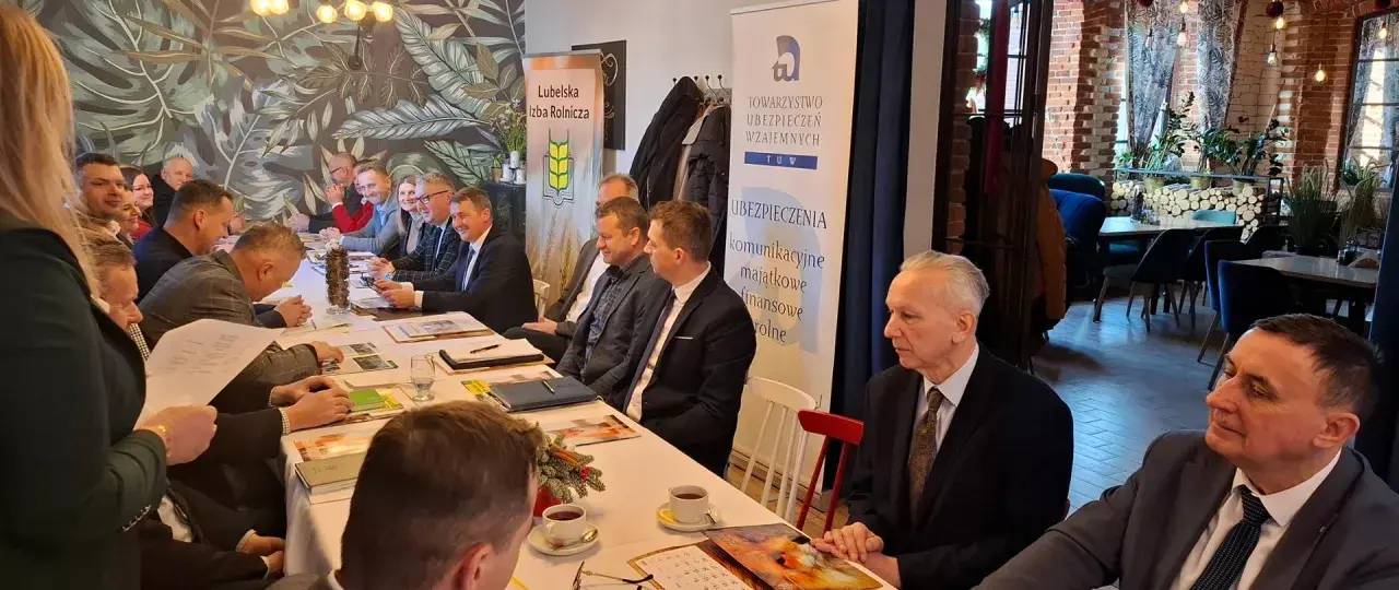 Ludzie siedzący przy stole podczas spotkania, na ścianie banery "Lubelska Izba Rolnicza" i "TUW Ubezpieczenia".