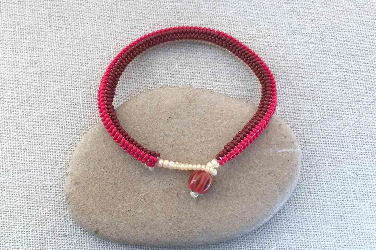 Braccialetto fatto a mano con nodi per braccialetti elastici, perline rosse e marroni, e una perlina centrale striata.