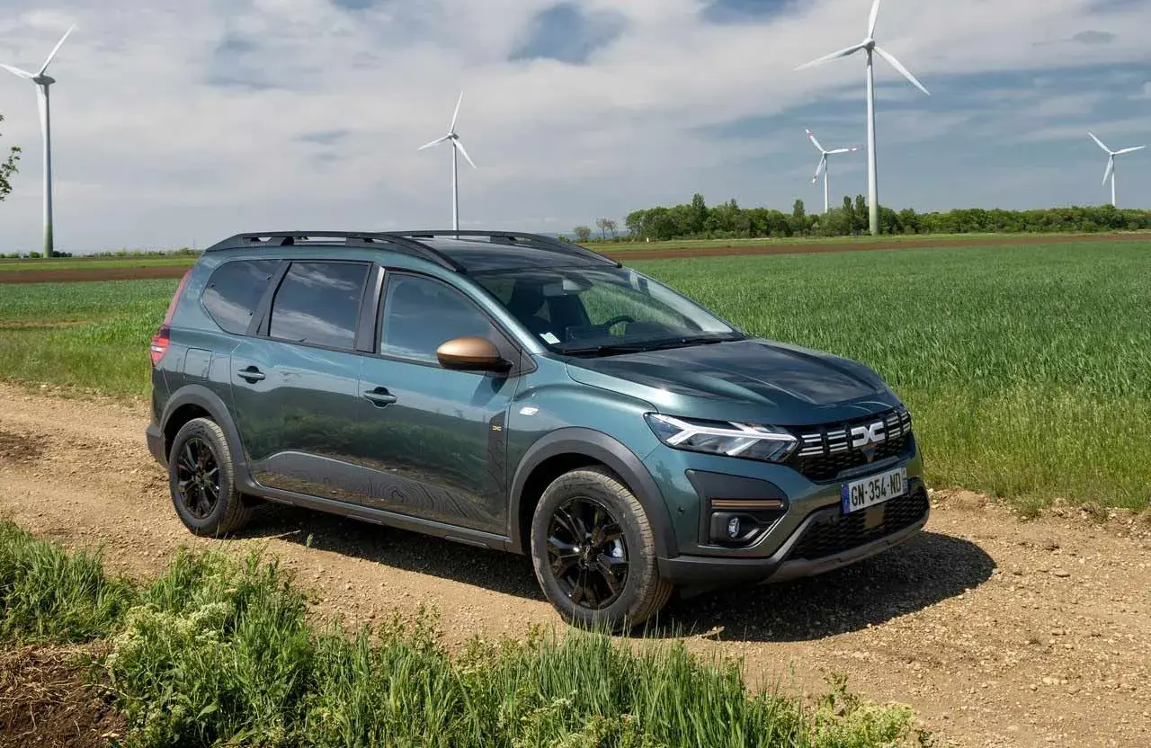 Dacia Jogger verde su sterrato, con pale eoliche sullo sfondo. Un'auto perfetta per un viaggio in autostrada con **GPL**.