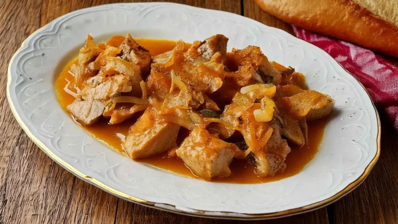Sabroso atún encebollado en una salsa dorada, servido en un plato blanco con borde dorado.