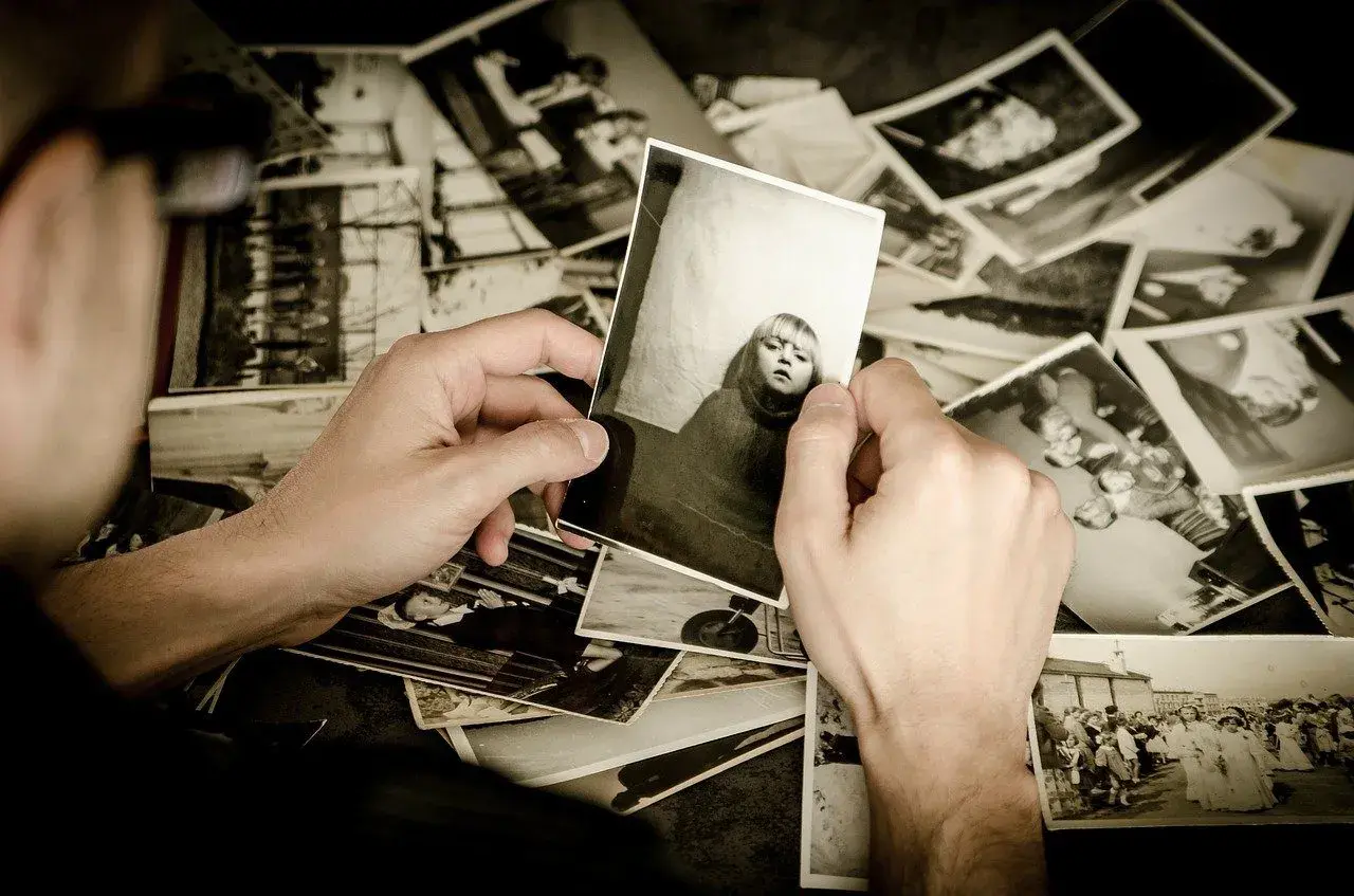 Mani che sfogliano un archivio foto, tenendo in mano una foto di una bambina. Ricordi che riaffiorano.