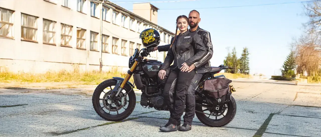 Para motocyklistów w skórzanych ubraniach siedzi na motocyklu Indian, obok stoi kask.