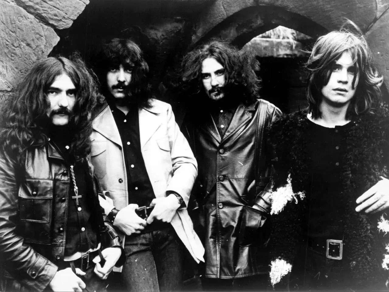 Czterech muzyków Black Sabbath, w tym wokalista, pozuje do zdjęcia w rockowych strojach.