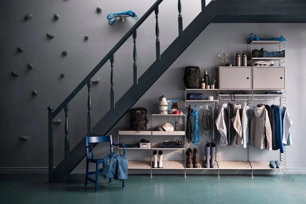Praktische Garderobe unter der Treppe mit Klettergriffen an der Wand, Jacken, Rucksäcken und Stiefeln.