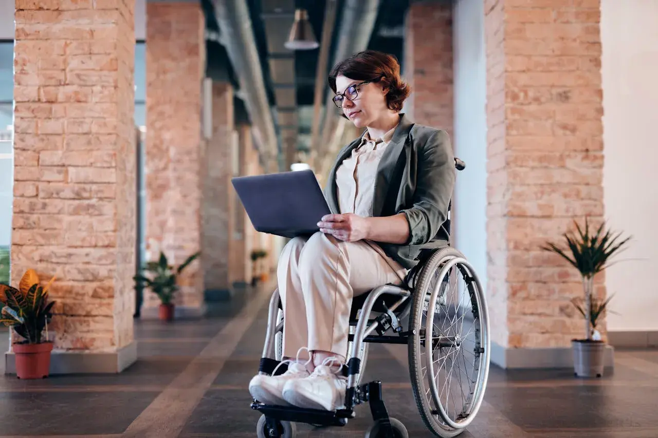 Kobieta na wózku inwalidzkim pracuje na laptopie w nowoczesnym biurze. Zlecenie na wózek inwalidzki zostało zrealizowane.