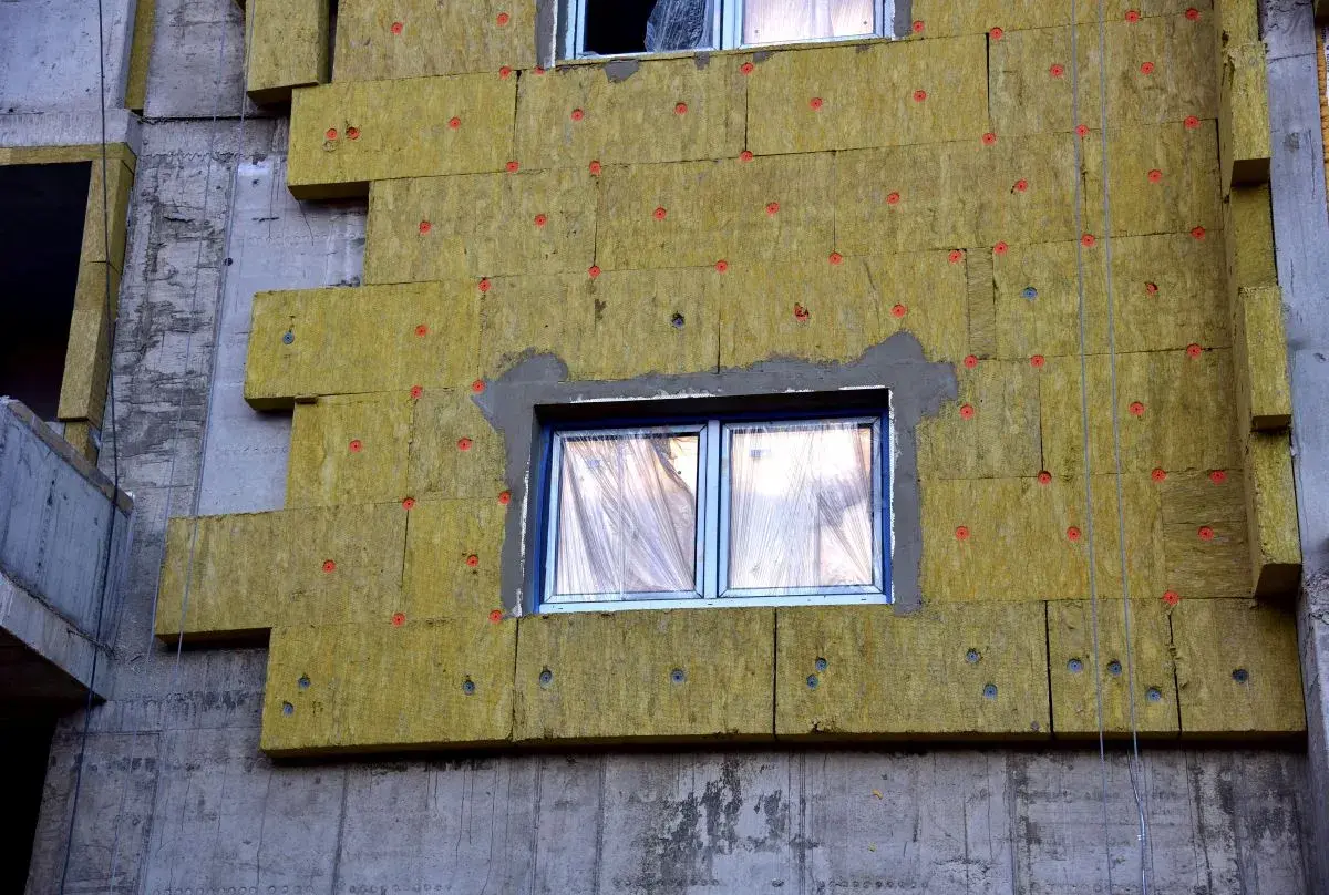 Pannelli isolanti gialli applicati al muro grezzo di un edificio in costruzione, creando un cappotto casa per l'isolamento termico.