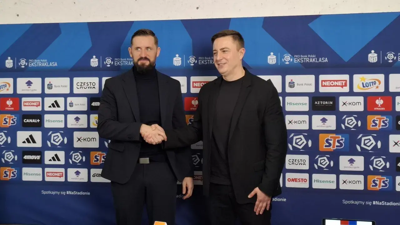 Dwóch mężczyzn w garniturach ściska sobie dłonie na tle ścianki sponsorskiej Rakowa Częstochowa. Zapowiada to nowe, ekscytujące transfery!