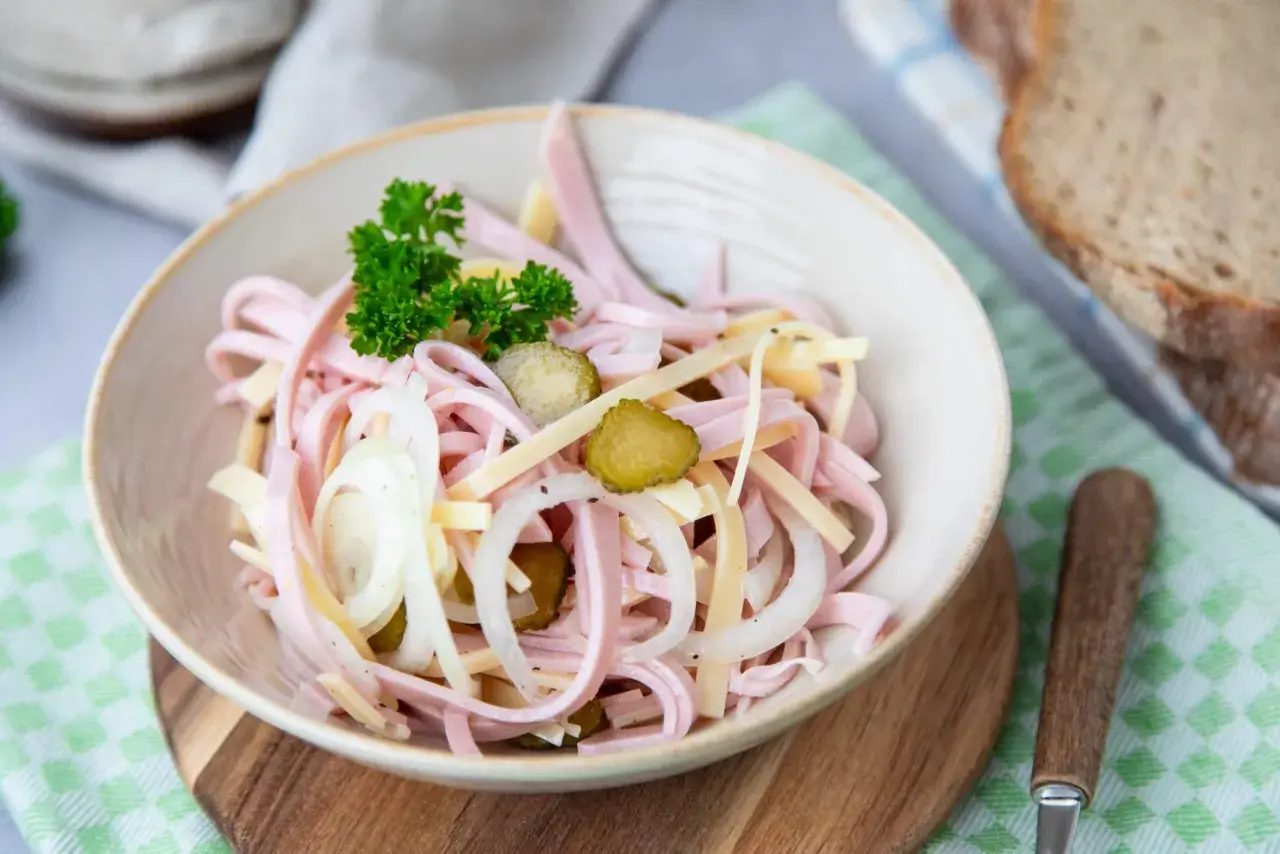 Ein köstlicher schweizer Wurstsalat mit Gurken, Zwiebeln und Käse, garniert mit Petersilie.