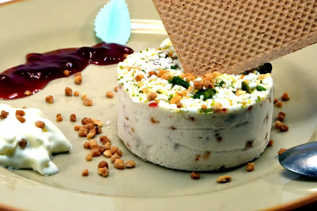 Un délicieux nougat glacé, parsemé de fruits secs et de pistaches, servi avec un coulis de fruits rouges et une touche de crème.