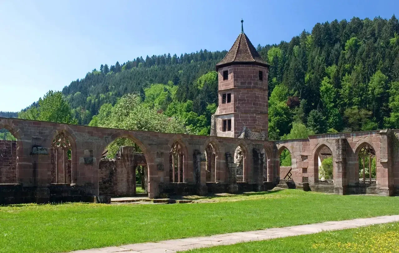 Ruinen eines evangelischen Klosters mit einem Turm im Hintergrund, umgeben von grünen Hügeln und Bäumen.