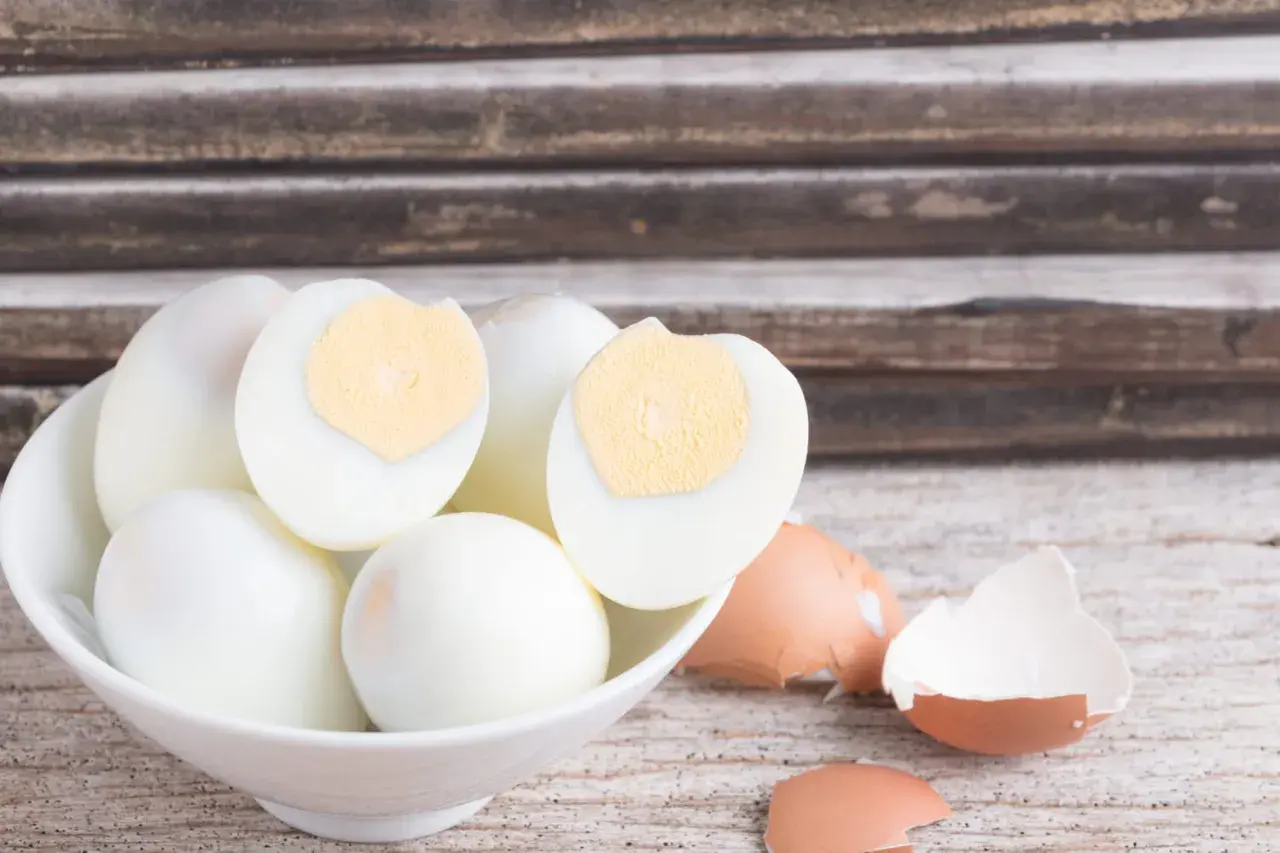 Un bol de blancs d'œufs durs, certains coupés en deux, prêts pour la conservation. Des coquilles d'œufs brisées à côté.