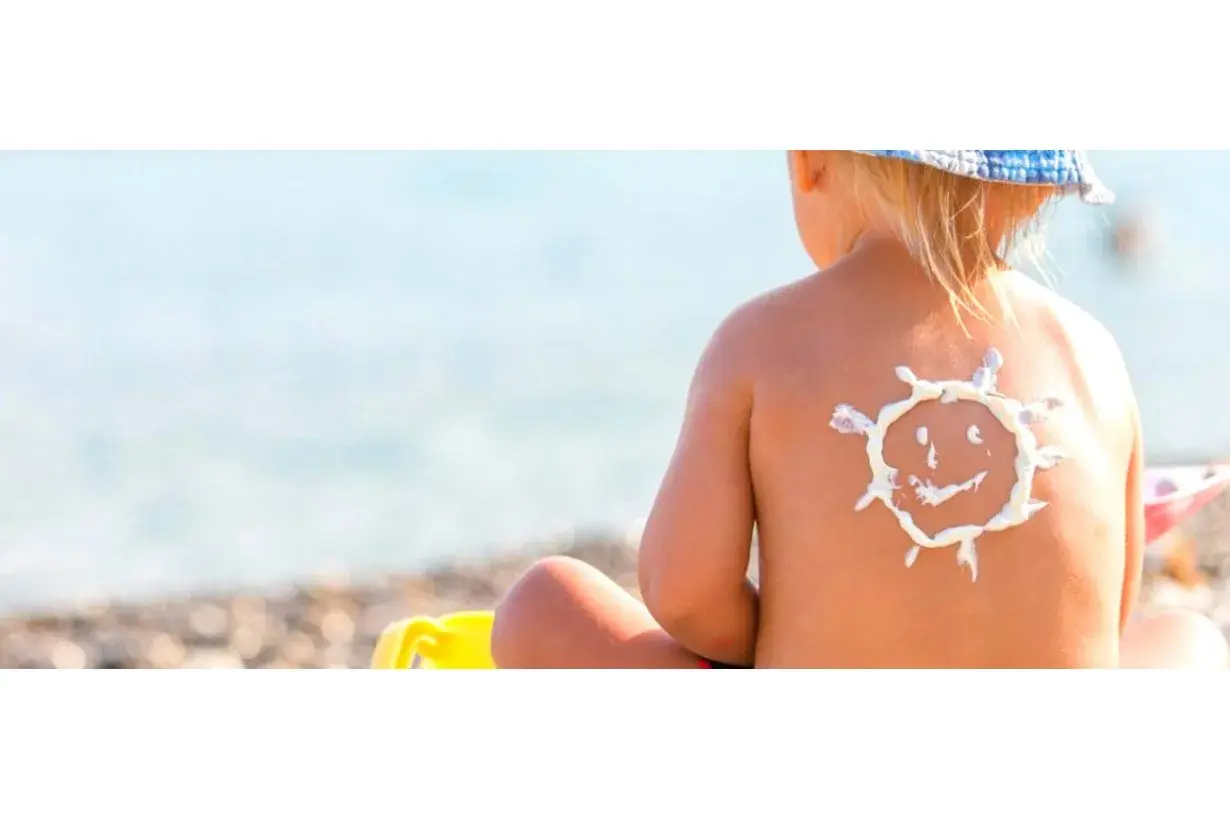 Bambino con crema solare a forma di sole sulla schiena, al mare. Protezione per la dermatite atopica e il sole.