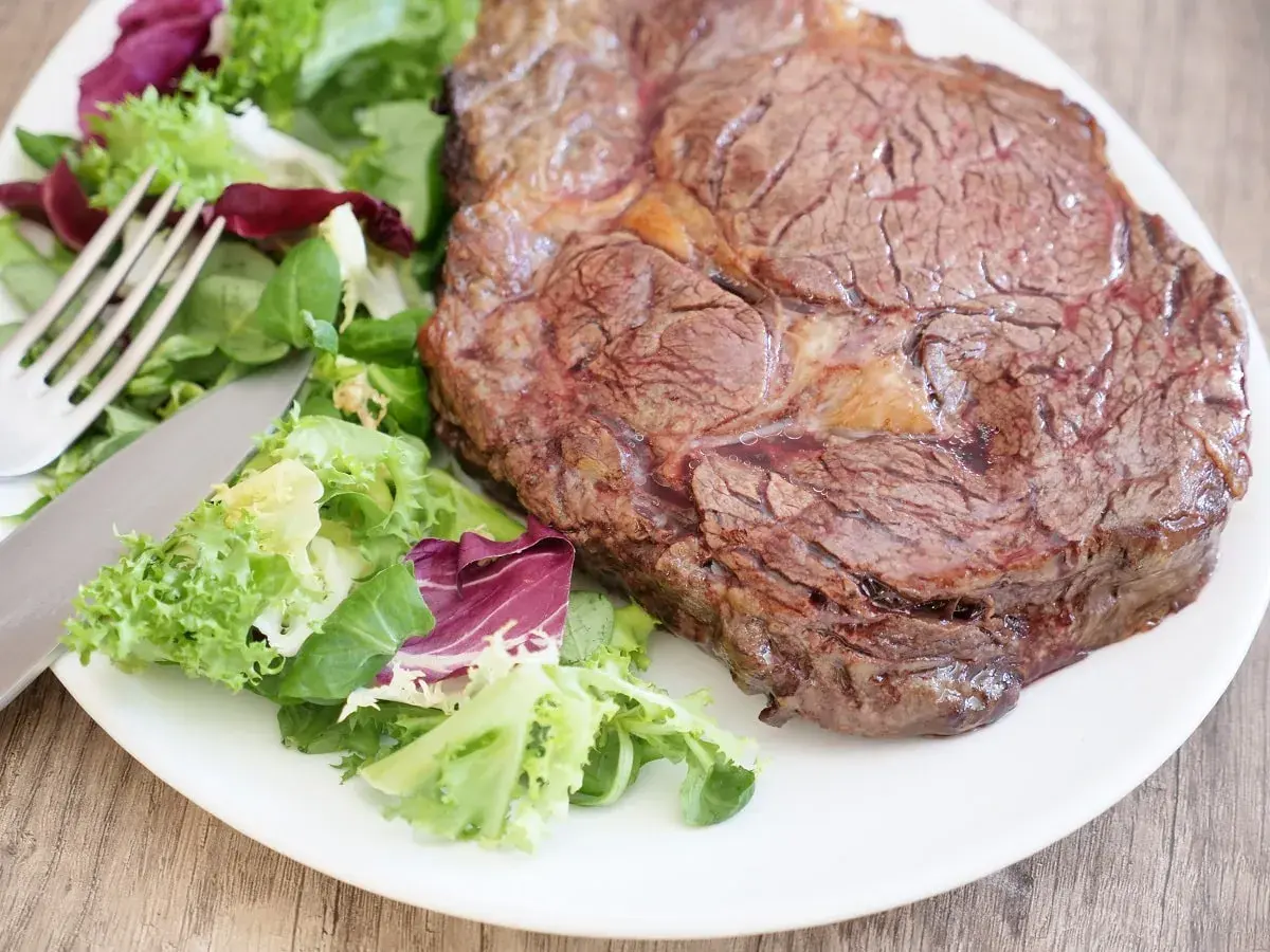 Une belle côte de bœuf, parfaitement saisie, accompagnée d'une salade fraîche. La cuisson est idéale pour un plat savoureux.