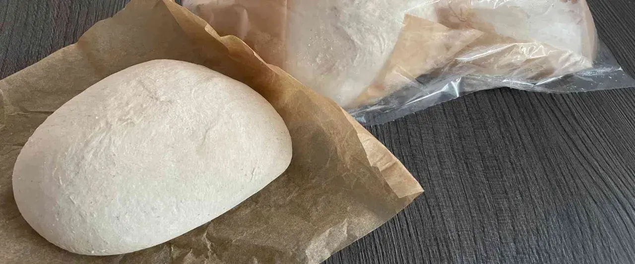 Frische Pizzaböden, bereit für das Pizzateig einfrieren. Einer liegt auf Backpapier, weitere sind in Folie verpackt.