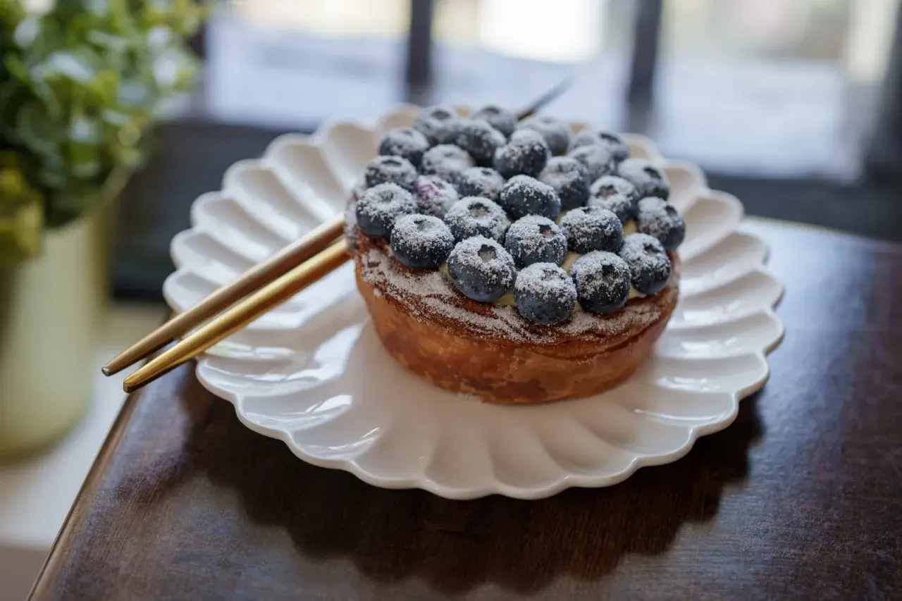Tarte myrtille Savoie, une gourmandise aux myrtilles fraîches saupoudrée de sucre glace, servie sur une assiette blanche.