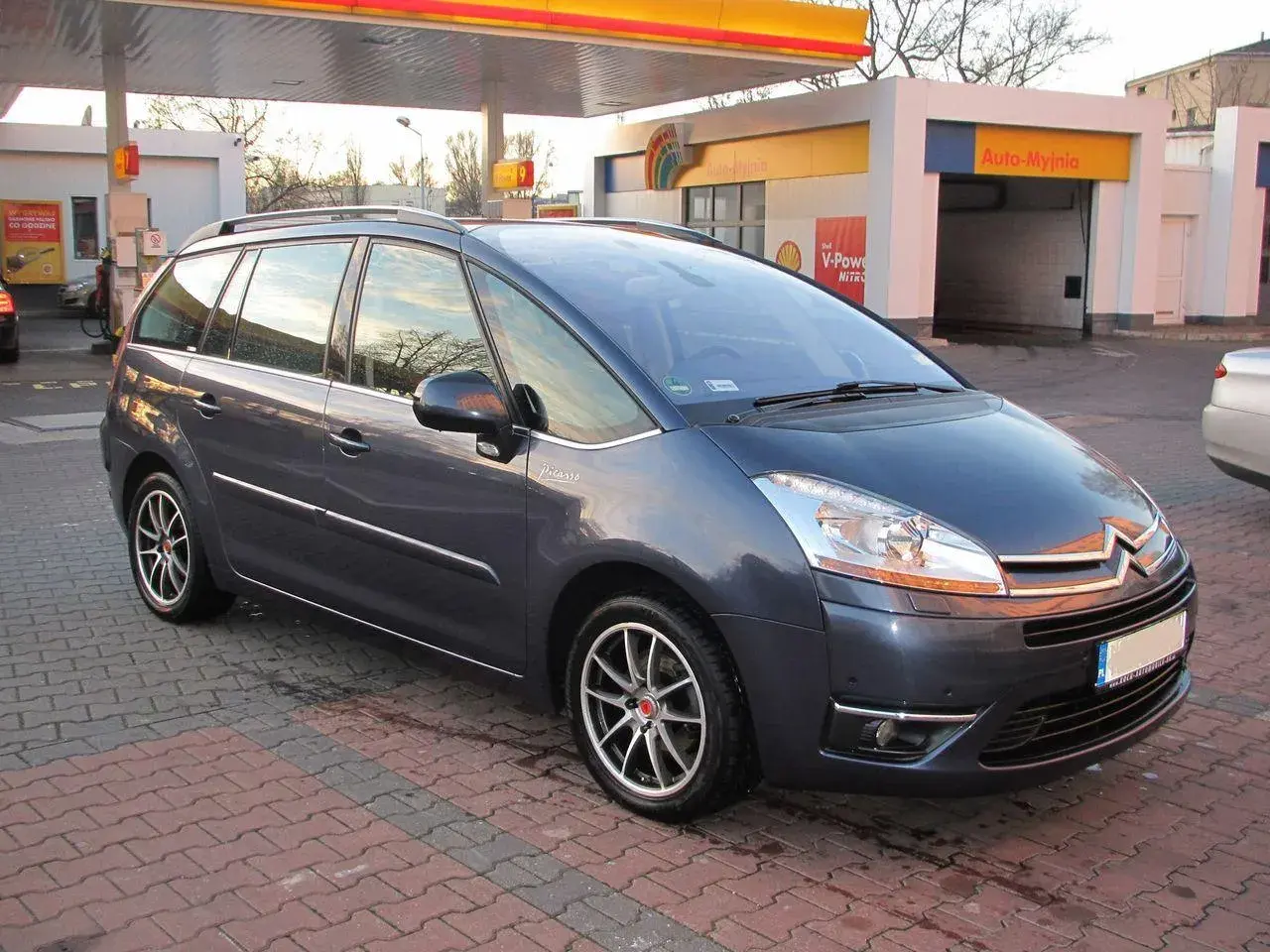 Ciemnoszary Citroen C4 Grand Picasso 2.0 HDI na tle stacji paliw.