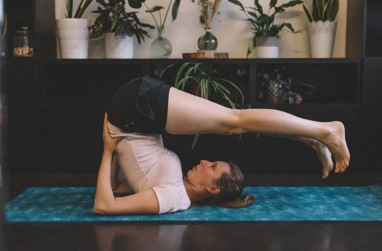Femme effectuant des étirements du dos sur un tapis de yoga bleu. Ses jambes sont levées et tendues au-dessus de sa tête.