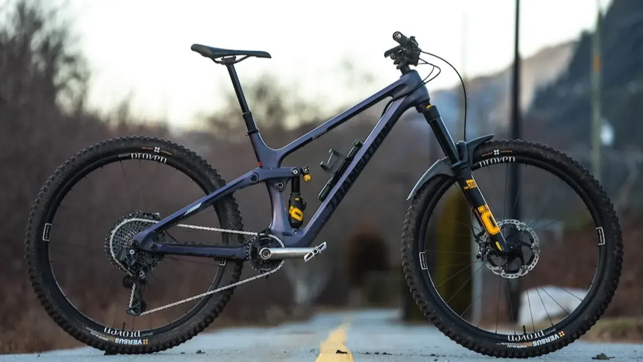 A dark purple full-suspension mountain bike with yellow accents sits on a road. Its components suggest a focus on performance, hinting at a competitive mountain bike weight for agile trail riding.