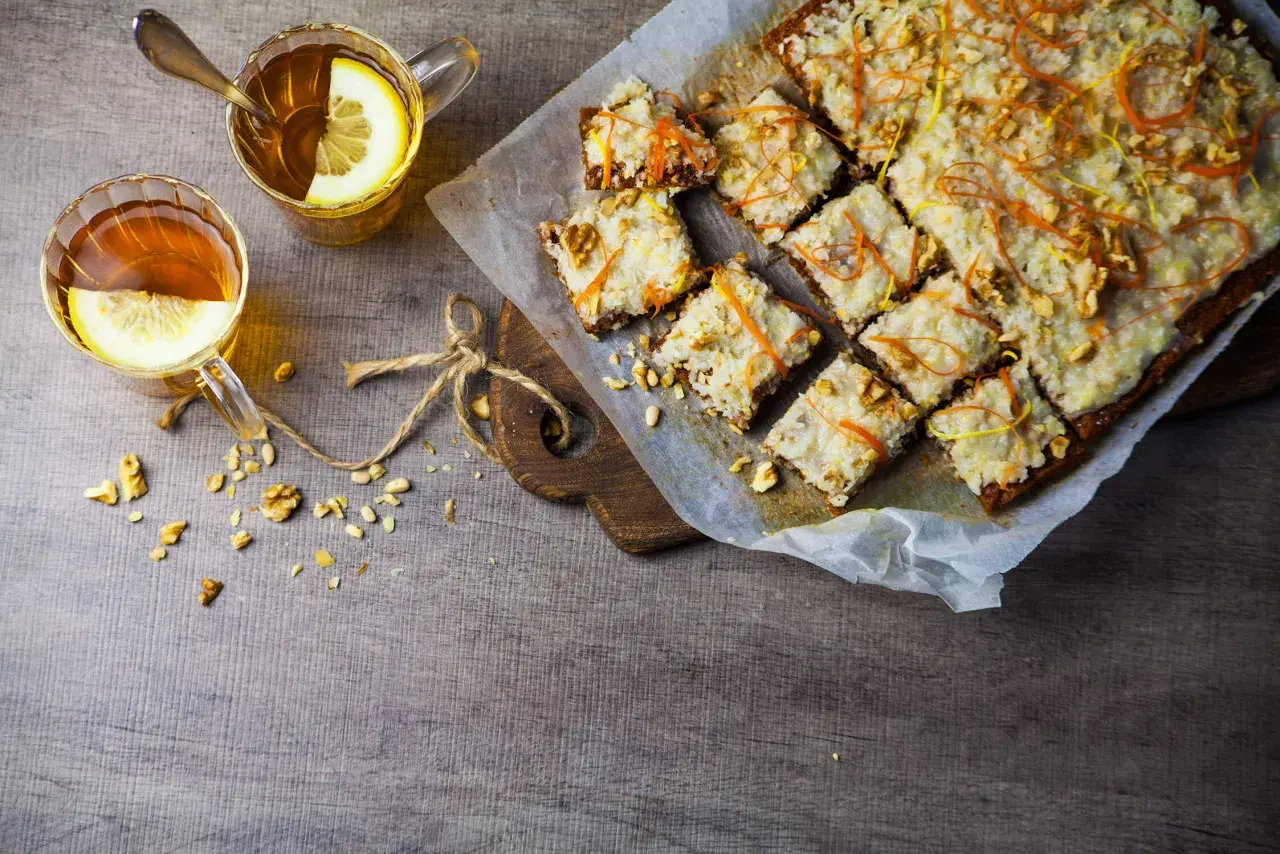 En härlig vegansk morotskaka med glasyr, nötter och citrusskal. Två koppar te med citron står bredvid.