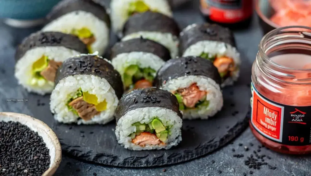Gotowe do jedzenia rolki sushi z łososiem i awokado, obok słoiczek marynowanego imbiru i miseczka czarnego sezamu – idealne składniki do sushi.
