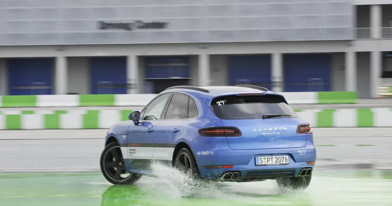 Niebieski Porsche Macan Turbo na mokrym torze Driving Center, rozpryskuje wodę. DSC co to? System stabilizacji toru jazdy.