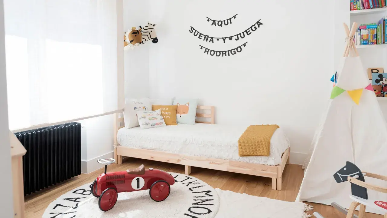 Un cuadro juego de niños con un tipi, cama, peluches y un coche de juguete rojo. "Aquí sueña y juega Rodrigo" decora la pared.
