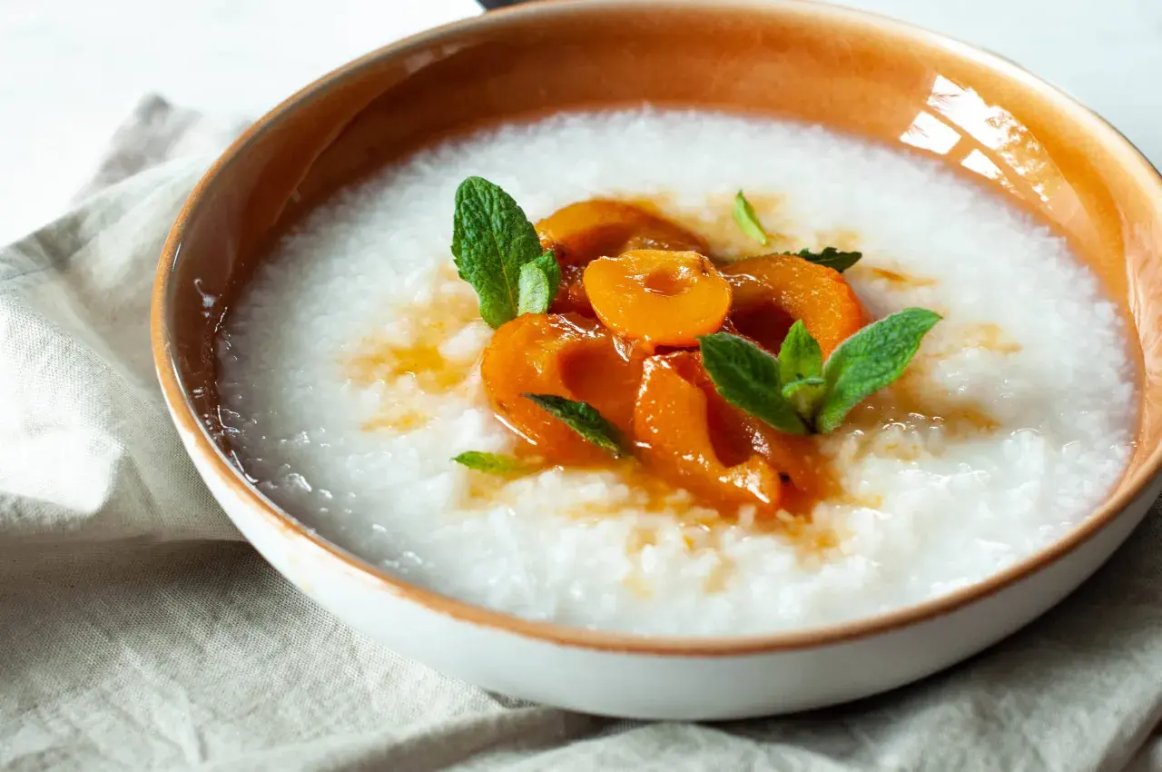 Miseczka z kremowym congee, ozdobiona kawałkami brzoskwini i listkami mięty.