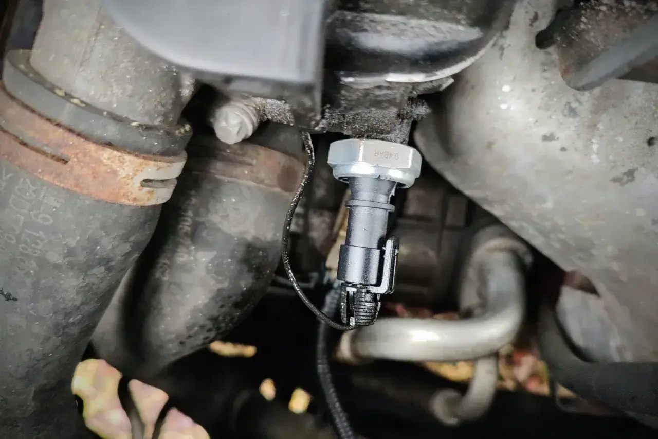 Czujnik ciśnienia oleju 2.0 TDI znajduje się w pobliżu metalowych rur i przewodów silnika.