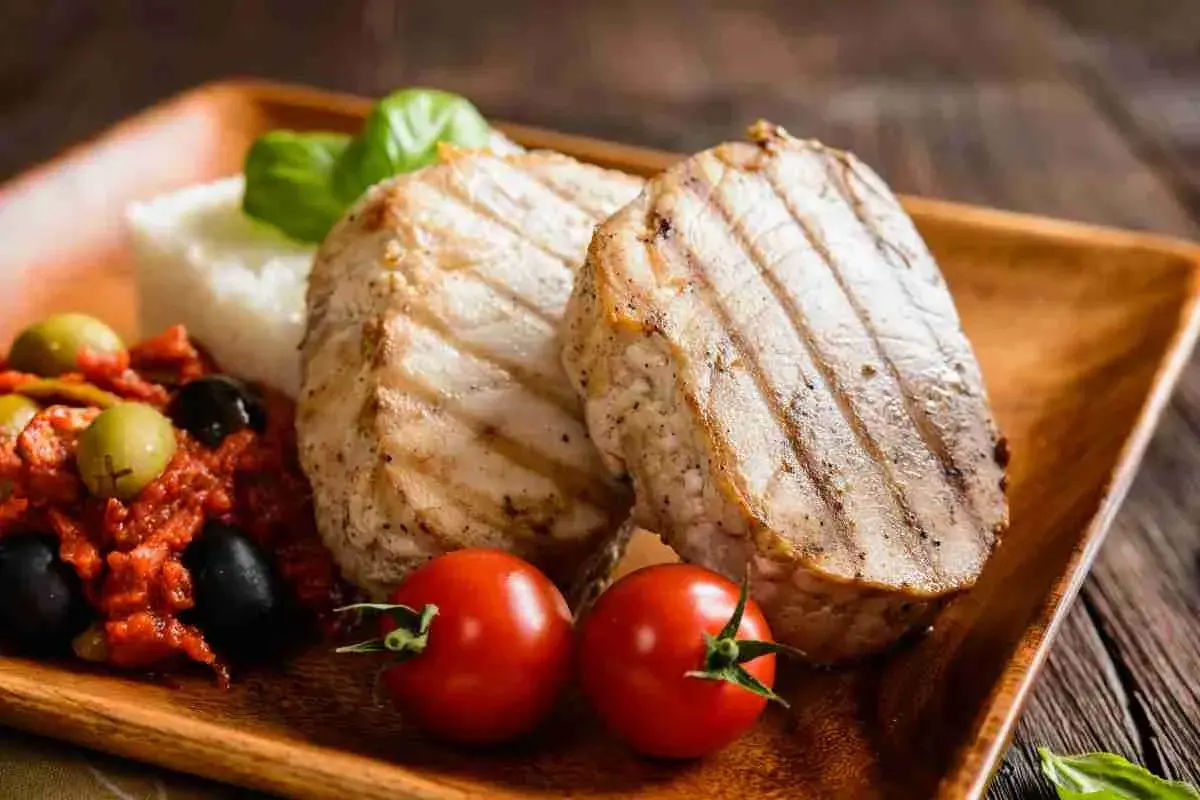 Delizioso tonno alla piastra con contorno di riso, pomodorini, olive e basilico su un piatto di legno.
