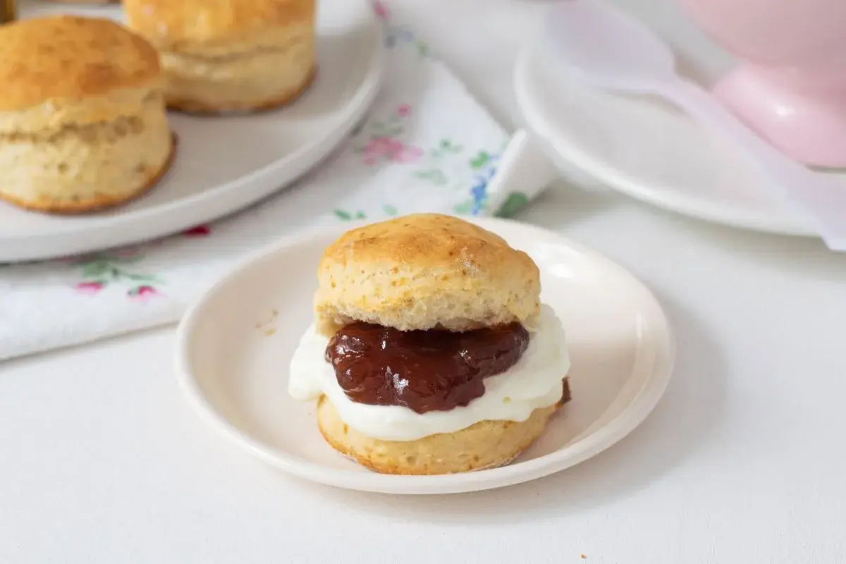 Un delicioso scone de reposteria inglesa, cubierto con crema y mermelada, listo para disfrutar.