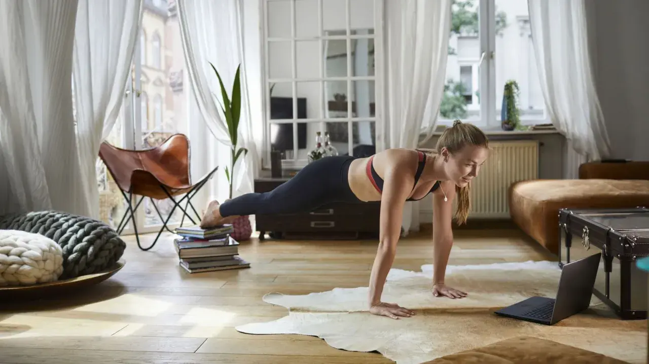 Femme en position de planche, suivant un entraînement de 7 minutes sur son ordinateur portable dans un salon lumineux.
