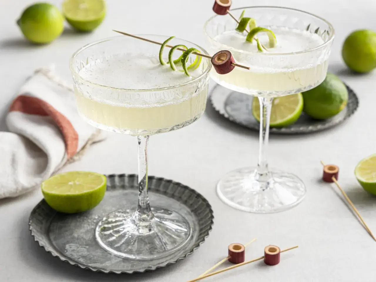 Zwei erfrischende Daiquiri Cocktails mit Limettenschale garniert, umgeben von frischen Limetten.