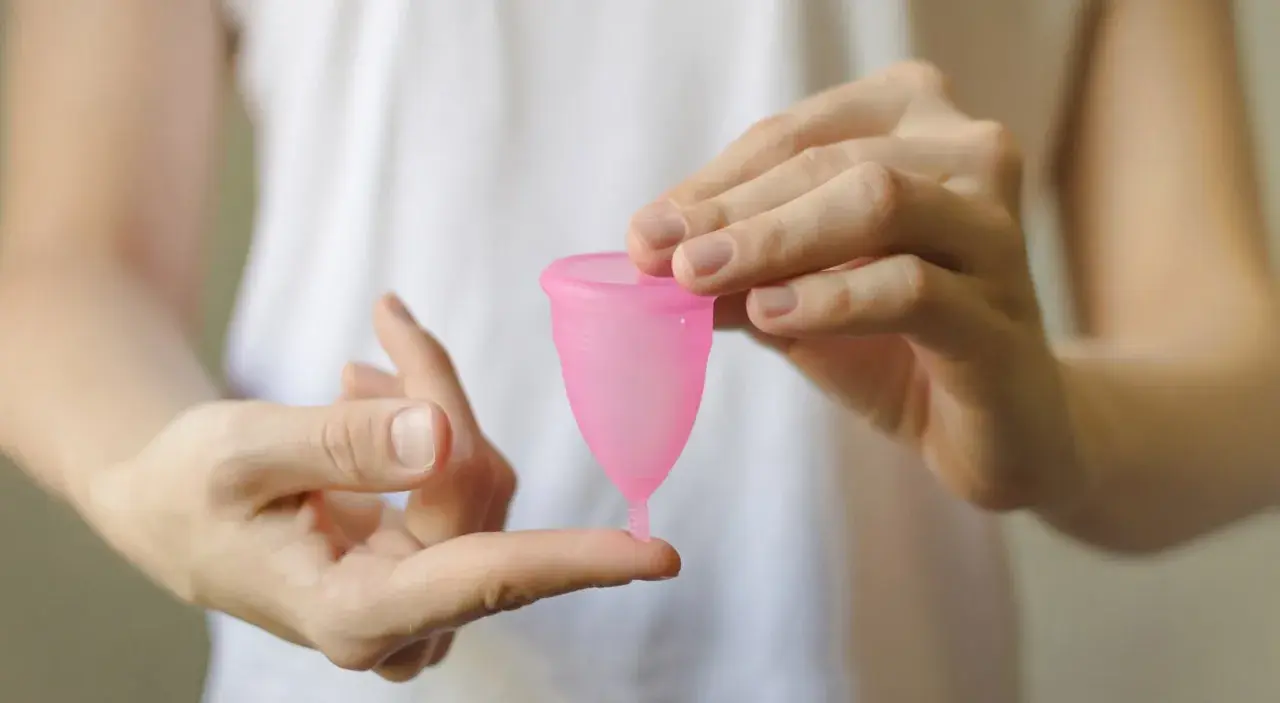 Manos sostienen una copa menstrual rosa. Aprende cómo poner la copa menstrual fácilmente.