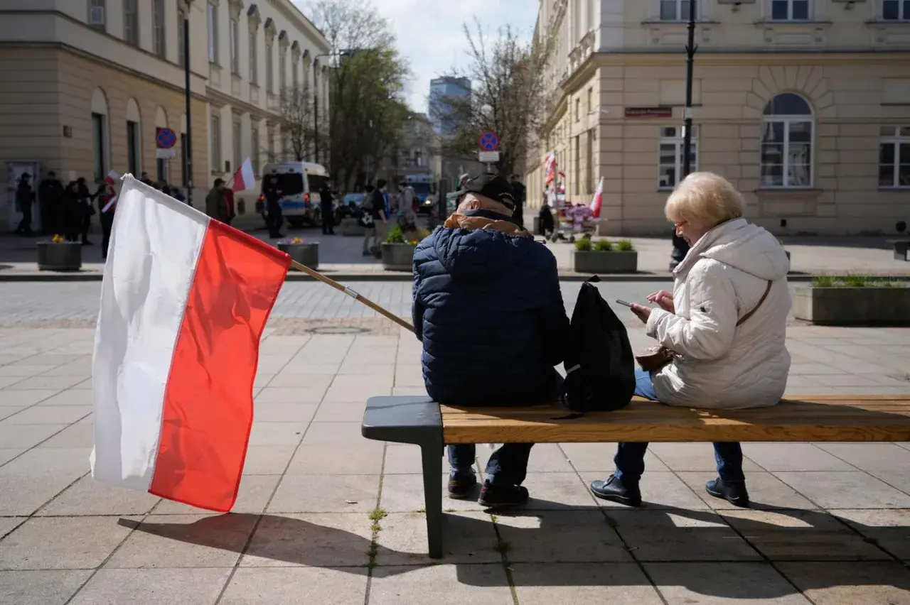 Zwei Personen sitzen auf einer Bank, eine polnische Flagge weht im Wind. Im Hintergrund sind Gebäude und Menschen zu sehen, die an einer Demonstration teilnehmen. Vielleicht geht es um den **ETF Polen**.