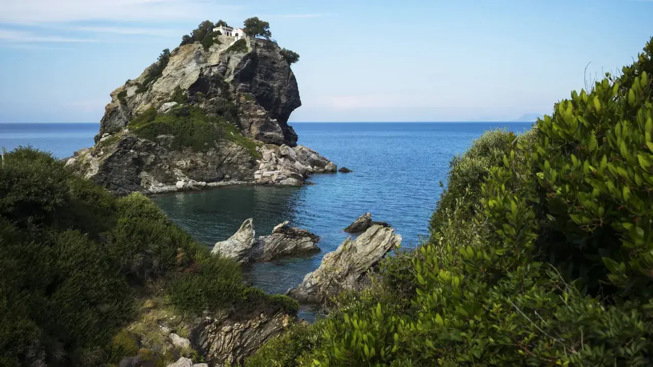 Felsige Klippe mit weißem Haus und Bäumen, umgeben von üppiger Vegetation und dem blauen Meer. Hier wurde Mamma Mia gedreht.