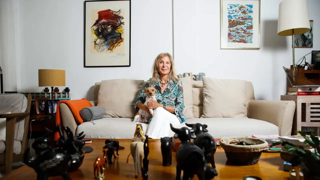 Pilar Eyre, sentada en un sofá con su perro, rodeada de arte y figuras de animales. Un vistazo a su mundo para el blog.