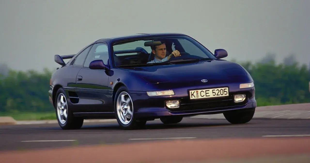 Mężczyzna prowadzi fioletowe Toyota MR2 SW20 po krętej drodze.