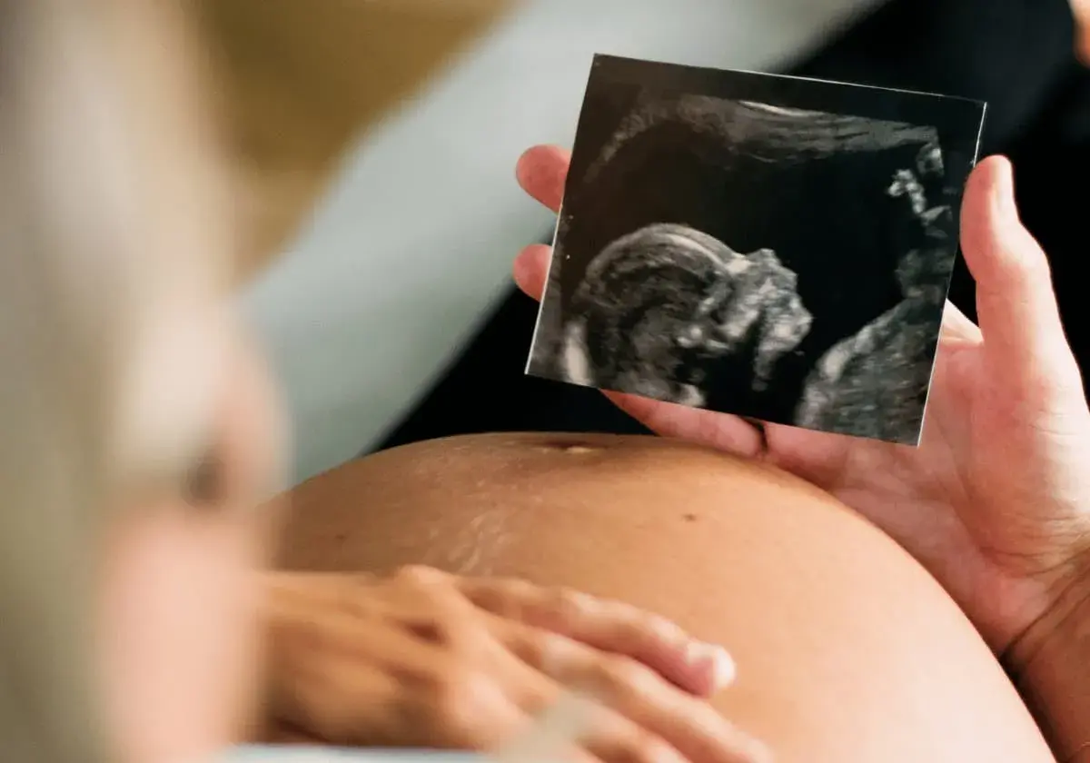 Gravid v 11, en hand håller upp ett ultraljudsfoto av ett foster. Trots oro för missfallsrisk, en stund av hopp.