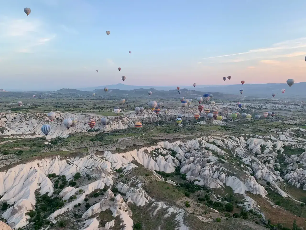 Setki balonów na gorące powietrze unoszą się nad skalistym krajobrazem Kapadocji o wschodzie słońca. To marzenie o podróżowaniu, które można zrealizować, szukając sposobów, jak tanio podróżować.