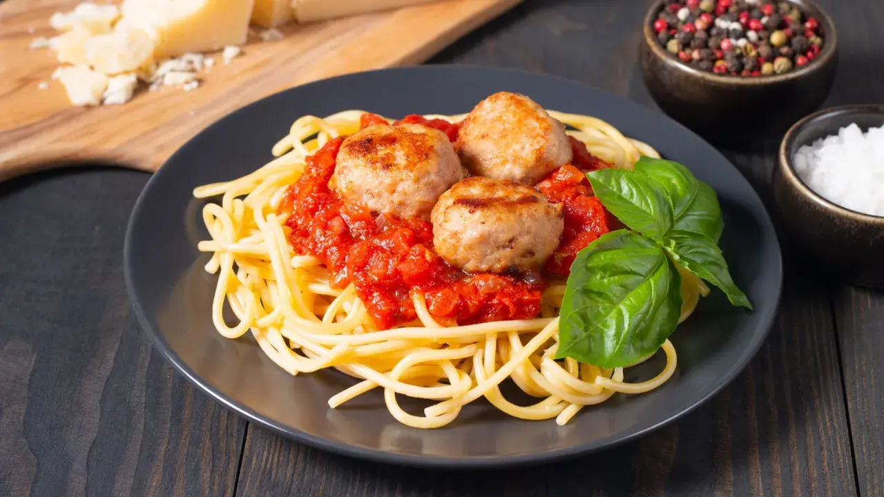 Spaghetti con tres jugosas polpette en salsa de tomate, decorado con albahaca fresca. Un plato clásico y delicioso.