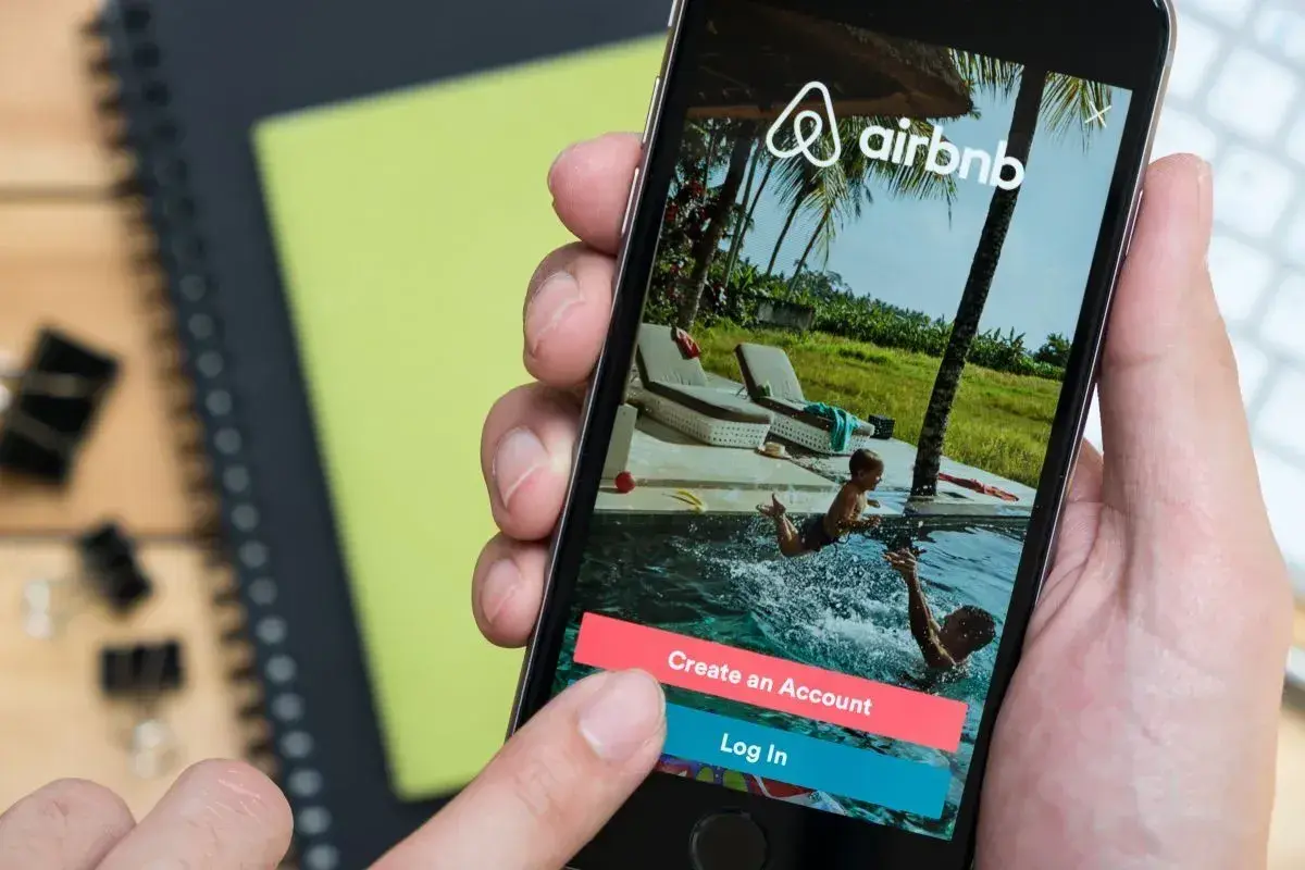 Dłoń wybiera opcję "Log In" na ekranie telefonu z aplikacją Airbnb. Czy Airbnb jest bezpieczne? To pytanie zadaje sobie wielu podróżnych.