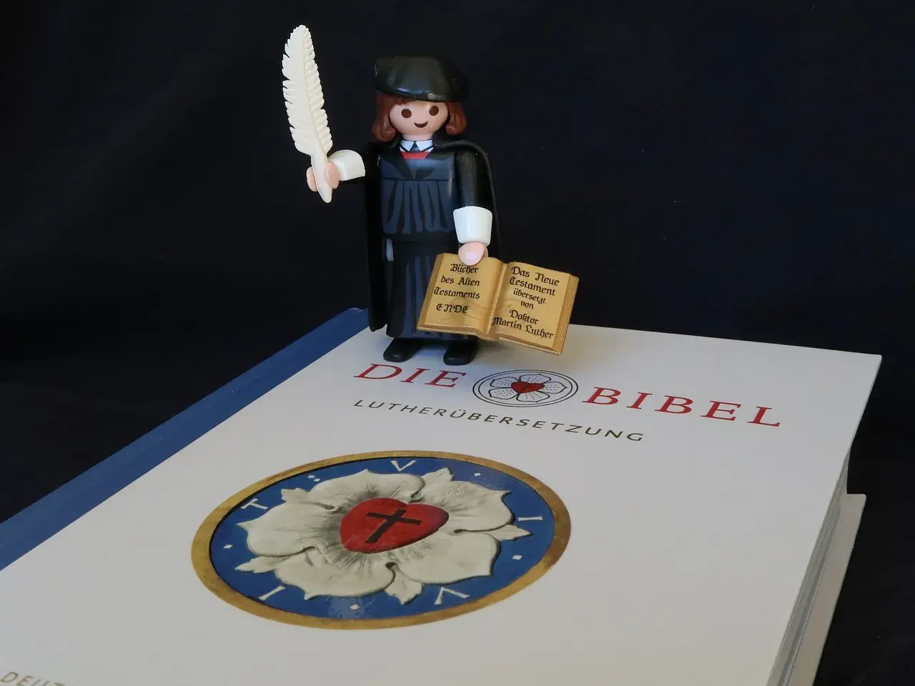 Playmobil-Figur mit Federkiel und Büchern, die den Unterschied zwischen Lutherbibel und katholischer Bibel symbolisiert.