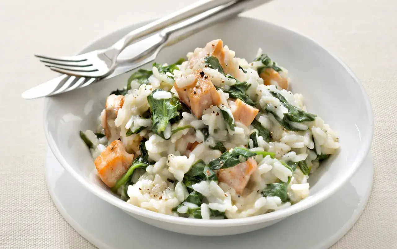 Un crémeux risotto épinard avec des morceaux de saumon. Un plat savoureux et coloré, prêt à être dégusté avec une fourchette et un couteau.