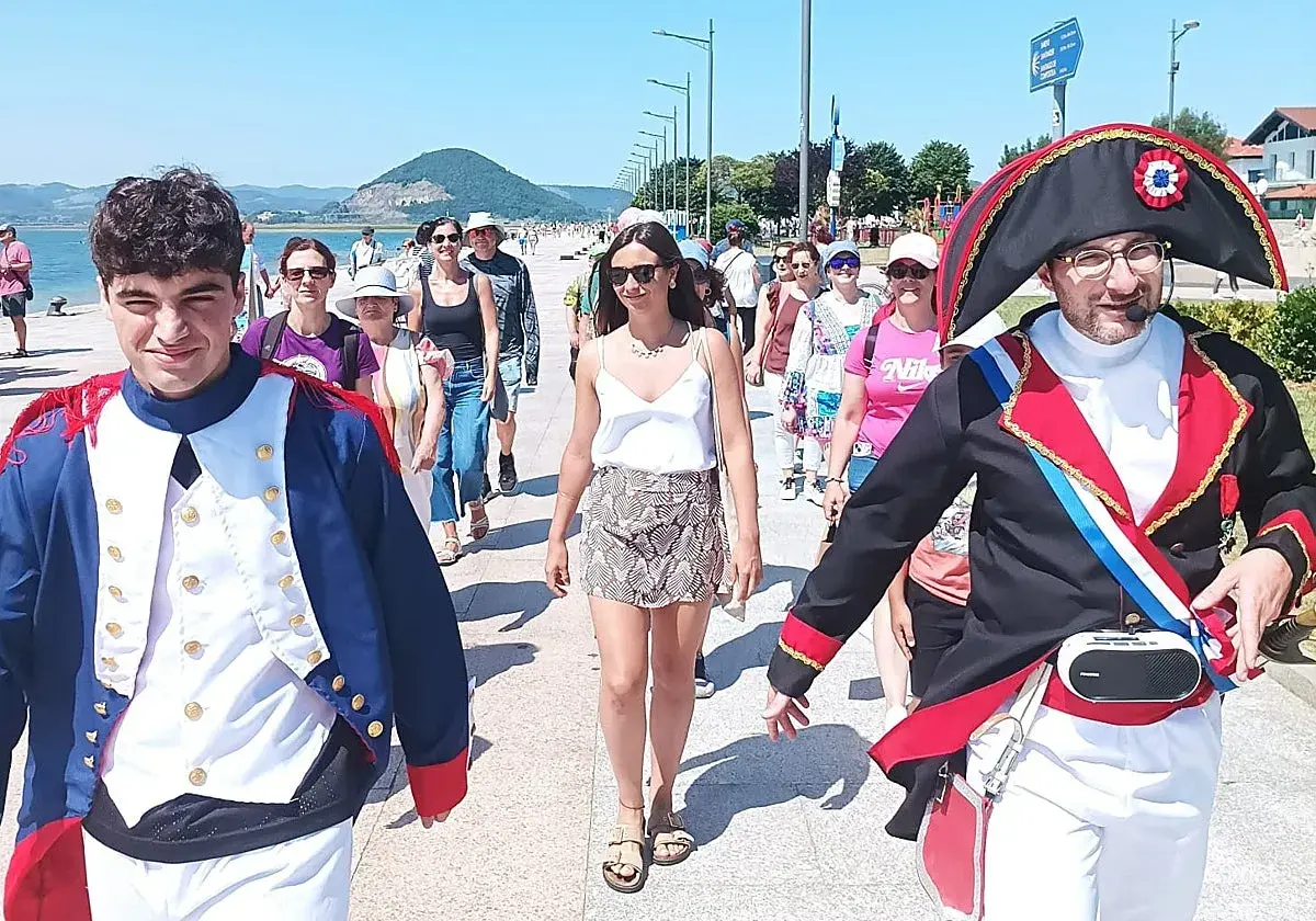 Gente pasea por el paseo marítimo de Santoña, algunos disfrazados, disfrutando del sol y el ambiente festivo.