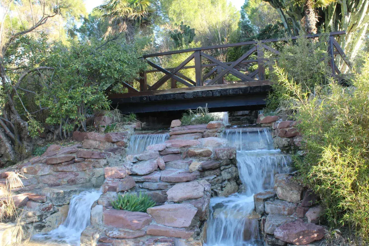 Puente de madera sobre cascadas en uno de los parques de Valencia. Naturaleza exuberante y rocas rojizas crean un paisaje idílico.