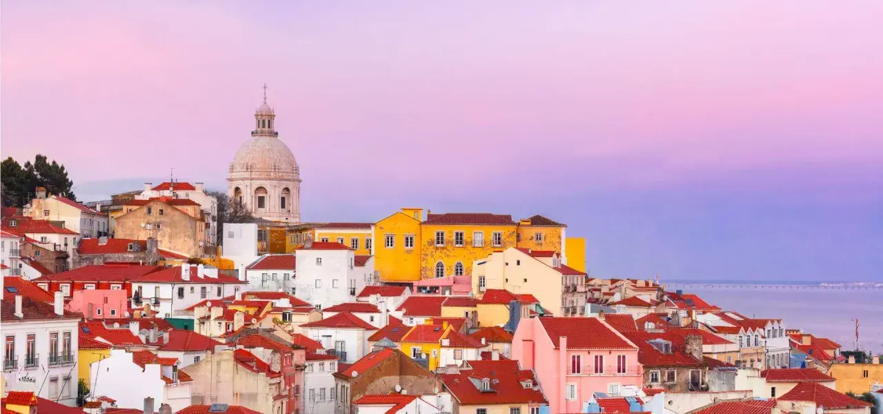 Tejado rojo y cúpula blanca bajo un cielo rosado. Un paisaje urbano que evoca las mejores experiencias en Lisboa.