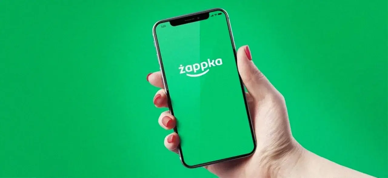 Dłoń trzyma smartfon z zielonym ekranem i logo Żappka. Sprawdzam, czy w Żabce są bilety autobusowe.