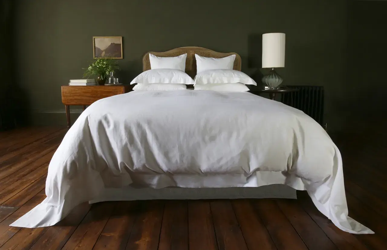 A white duvet cover, resembling a plush bedspread, drapes over a neatly made bed, contrasting with the crisp bed sheet visible beneath.