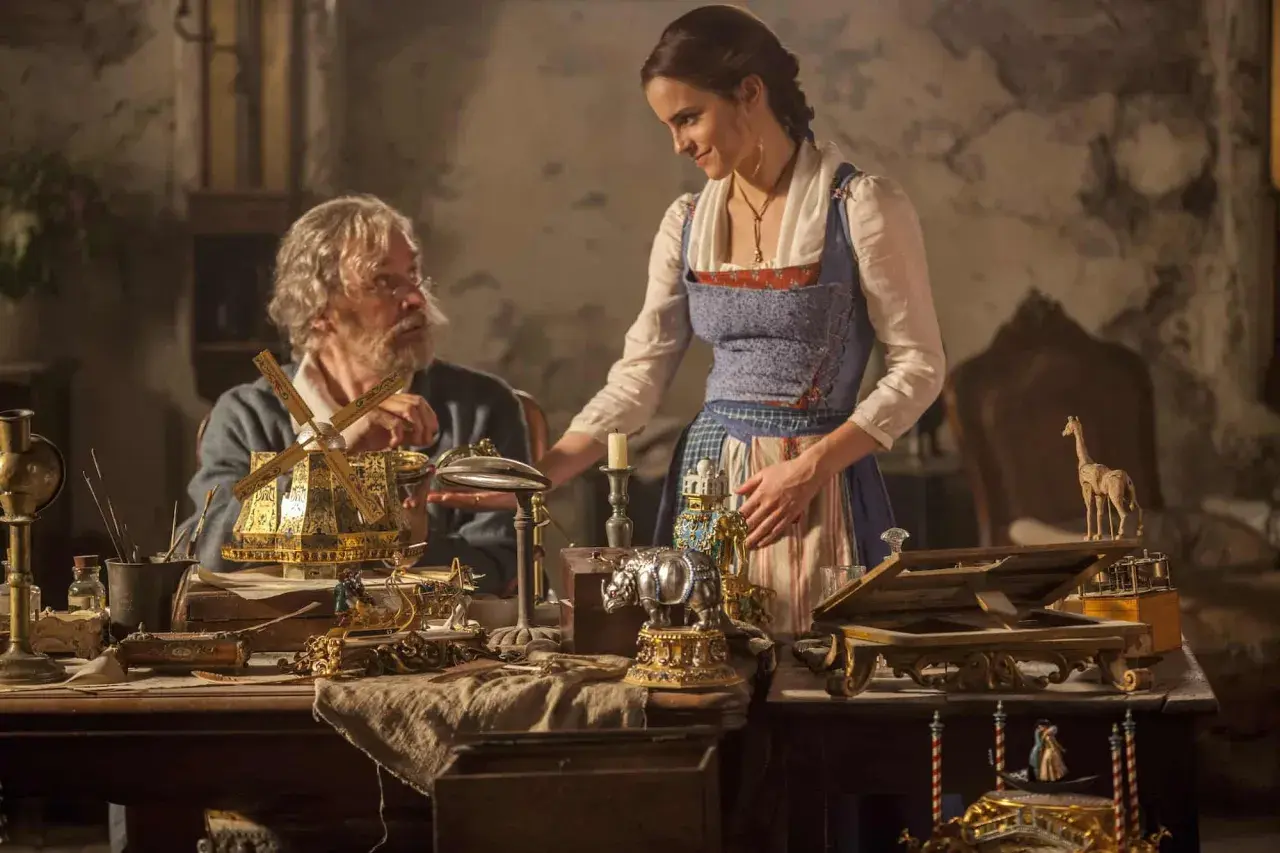 Bella y su padre, Maurice, observan un intrincado molino de viento dorado. La escena evoca la magia de "la bella y la bestia".