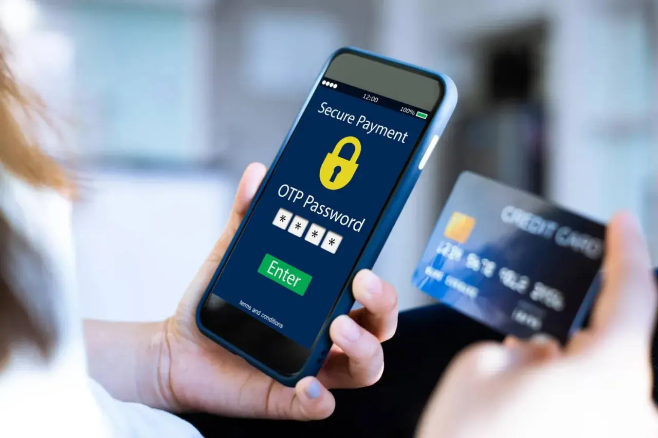 Mano sostiene un teléfono con pantalla de pago seguro y código OTP, junto a una tarjeta de crédito. El **sms certificado** confirma la transacción.